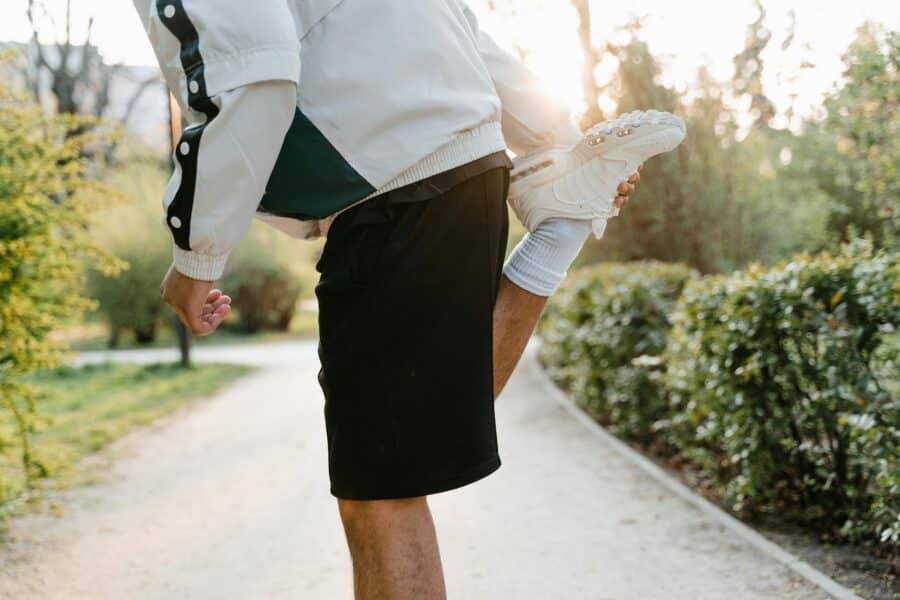 Adult lifting a child wearing white sneakers along a sunlit park path